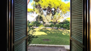 An open door leading to a courtyard with a large tree and a brick pathway. - Albufeira Açoteias Villa by Homing (Albufeira)