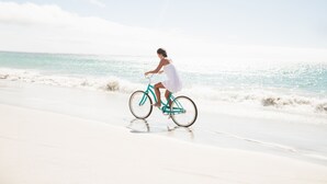 Uma pessoa andando de bicicleta na praia, com o oceano ao fundo.