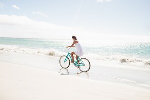 A woman on a bicycle on a beach with the ocean in the background.
