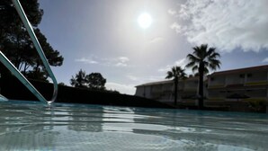 En swimmingpool med en klar vandoverflade der spejler solen og de omkringliggende træer.