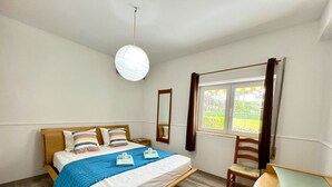 Et soveværelse med seng, stol, vindue og en hængende lampe.