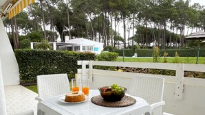 Et hvidt bord med en skål frugt, et glas appelsinjuice og en kage på en balkon med hvide stole.
