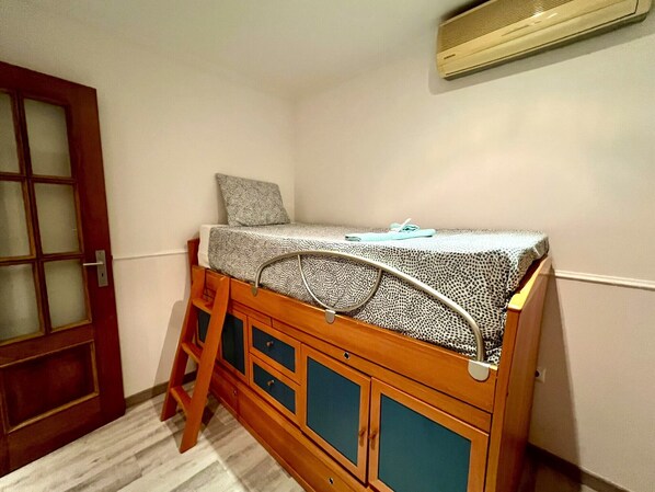 Una habitación pequeña y funcional con una cama nido de madera, una escalera y una puerta con paneles de vidrio esmerilado.