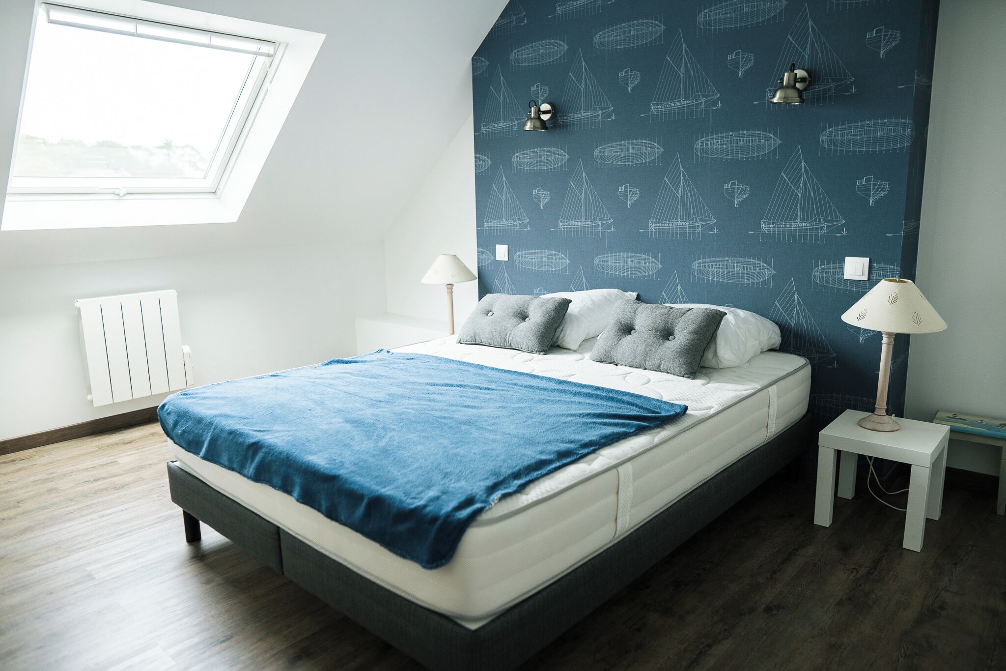 A bedroom with a bed, two bedside lamps, a window, and a radiator.