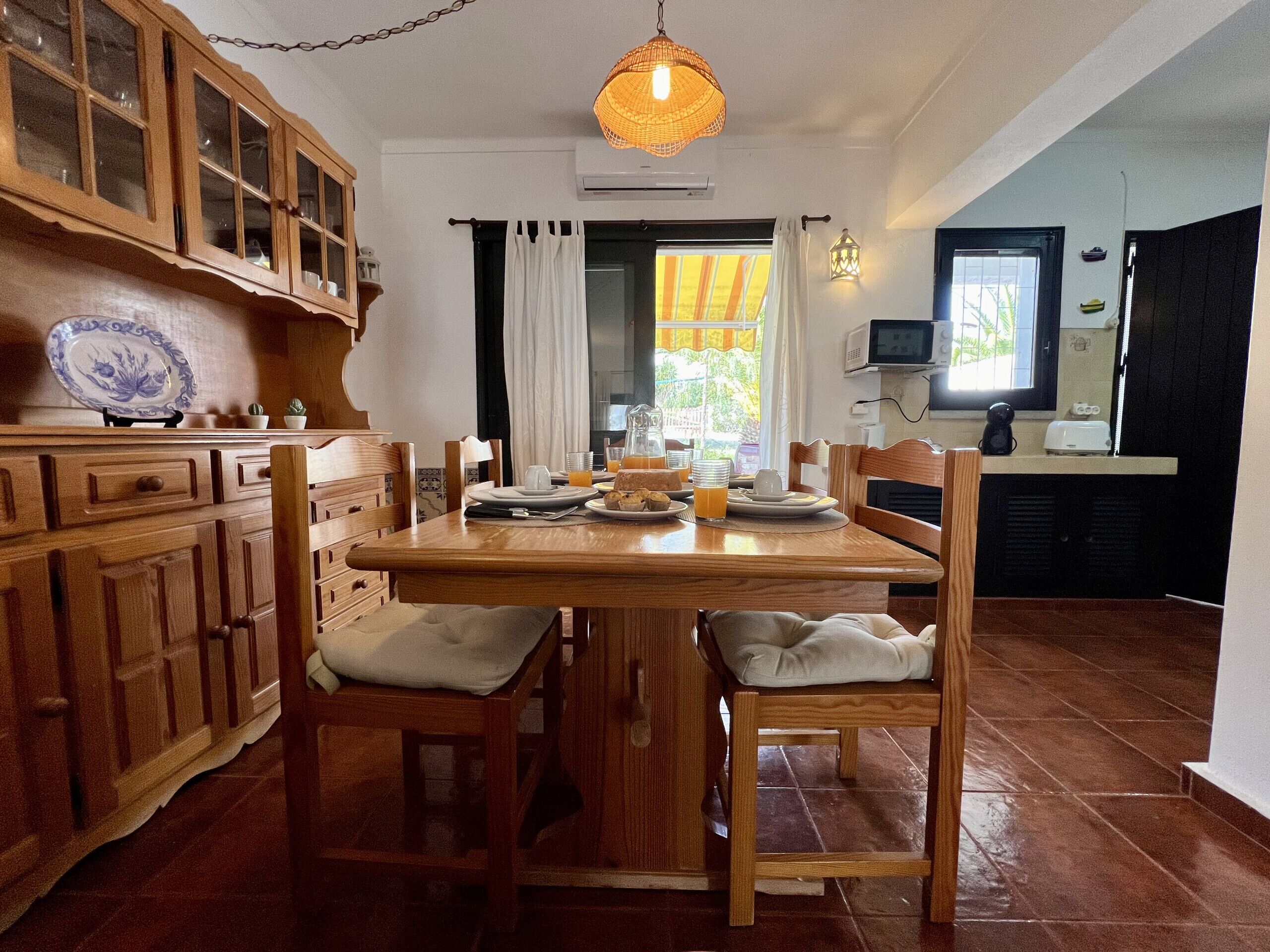 Una mesa de comedor de madera con sillas, una lámpara colgante y una cocina con armarios y un microondas.