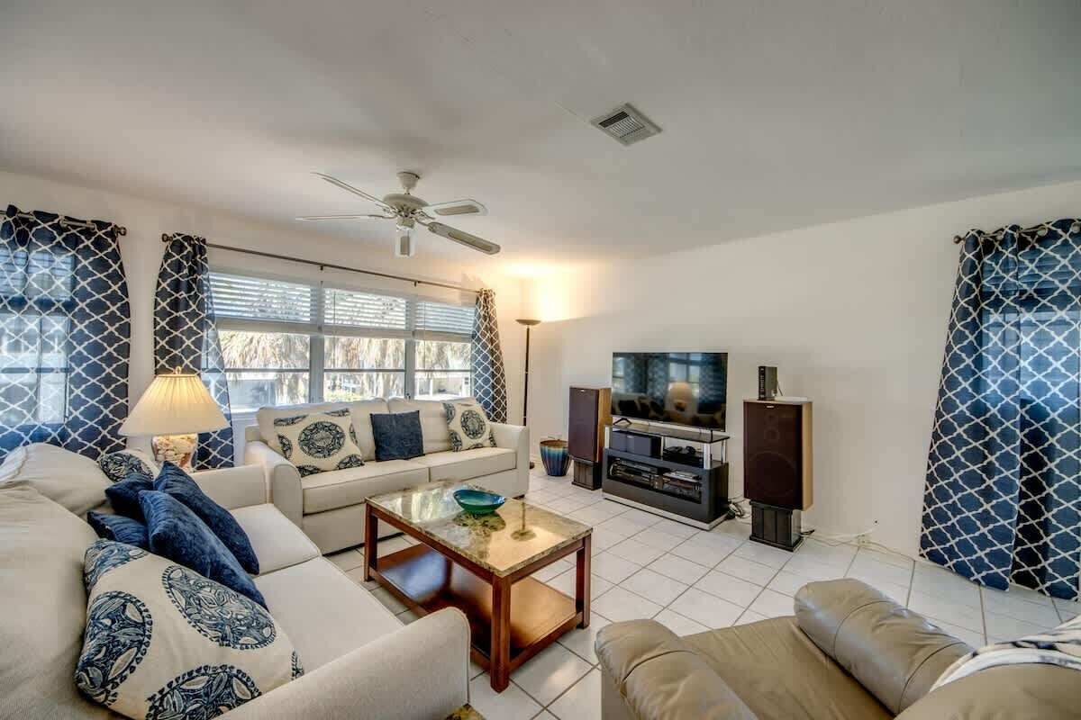 Una sala de estar con sofá, mesa de centro, televisor, parlantes y ventilador de techo.