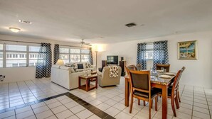 A living room with a sofa, a dining table with chairs, a TV, and a fireplace. - 190 Anchorage Unit A Spacious Unit near Beach (Fort Myers Beach)
