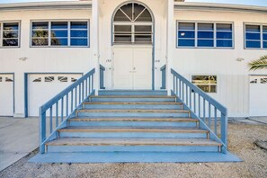 Un edificio con una entrada central, dos puertas de garaje y una escalera que sube a la entrada.