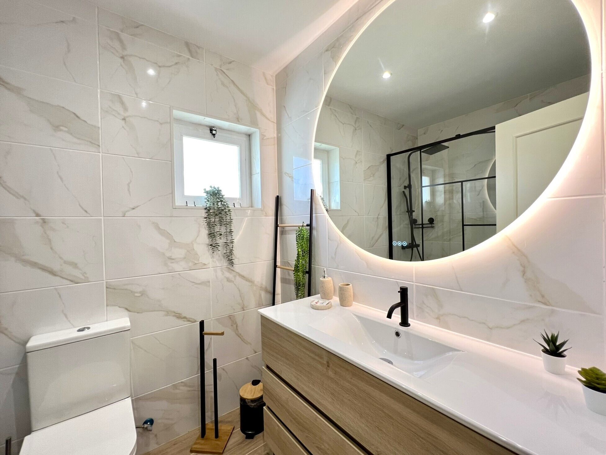 A modern bathroom with a marble backsplash, a large mirror, a toilet, a sink, and a shower area.