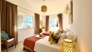 A bedroom with a bed, a bedside table, a lamp, a chair, and a view of the outdoors. - Vilamoura Brightness Villa by Homing (Loulé)