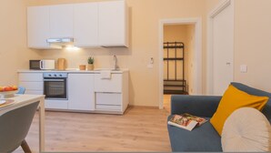 Un espacio habitable compacto con kitchenette, comedor y zona de estar con sofá y cojines.