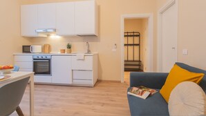 Un espacio habitable compacto con kitchenette, zona de comedor y un sofá con una revista.