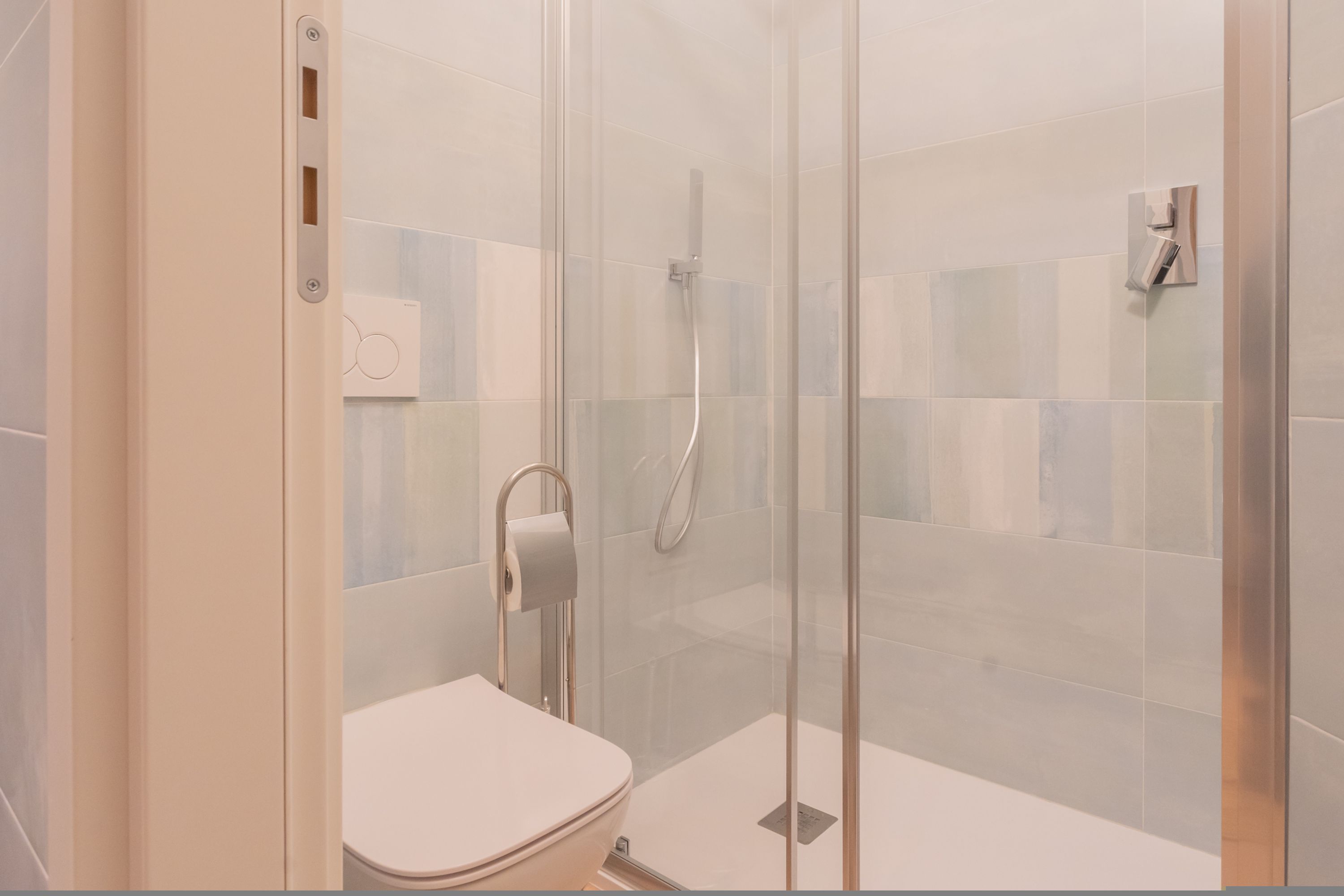 A modern bathroom with a glass-enclosed shower, a toilet, and a towel dispenser.