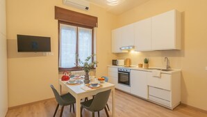 Cocina compacta con armarios blancos, un microondas y un lavamanos. Hay una mesa de comedor con sillas y un florero con flores.