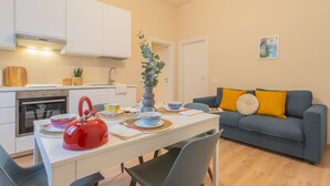 Una cocina moderna con armarios blancos, un hervidor rojo y una mesa de comedor para dos.