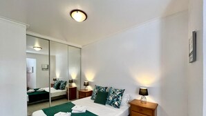 Ein modernes Schlafzimmer mit einem großen Bett, zwei Nachttischen, einem Spiegel und einer Deckenleuchte.
