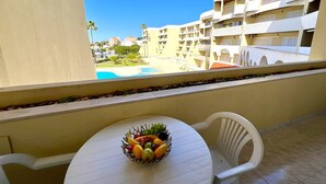Ein Balkon mit Tisch und Stühlen, einer Obstschale und Blick auf einen Pool und Gebäude.