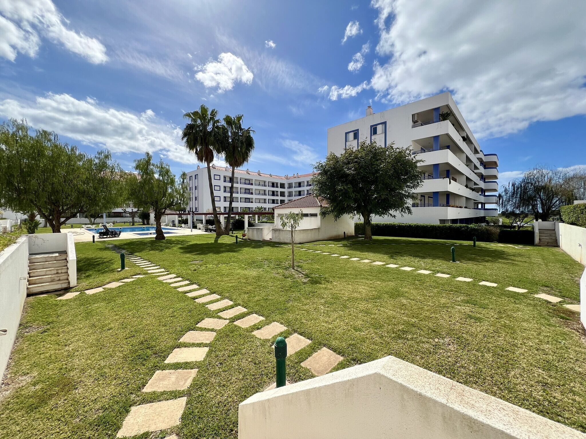 A modern building with multiple balconies, a swimming pool, and a well-maintained lawn with a stone pathway.