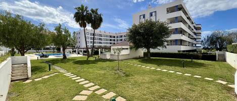 A modern building with multiple balconies, a swimming pool, and a well-maintained lawn with a stone pathway.