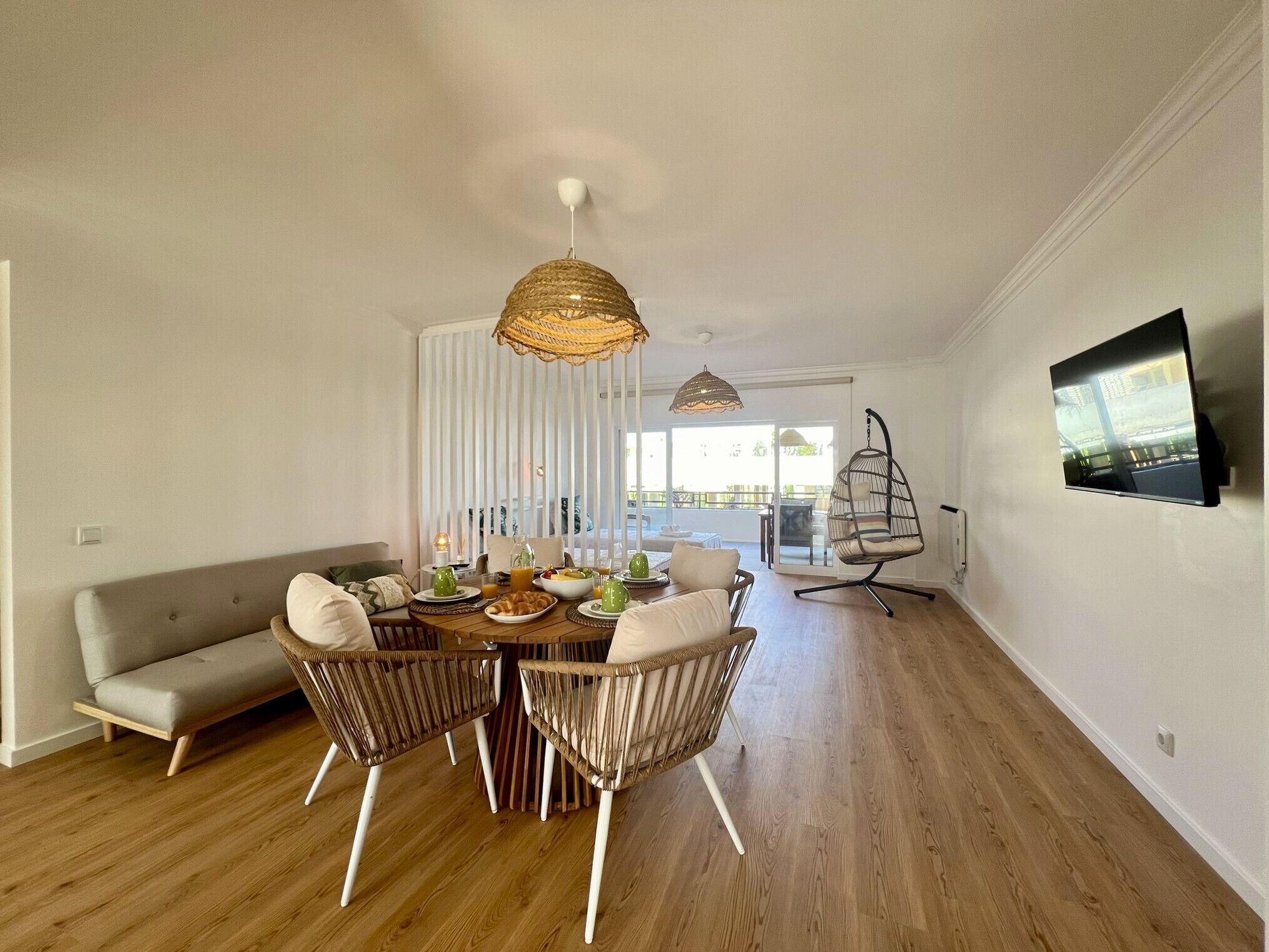 Un comedor moderno con una mesa de madera, sillas de mimbre y una lámpara colgante.