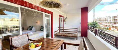 A balcony with a wooden table, a bowl of fruit, and a bench.
