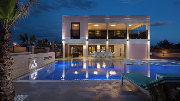 A modern two-story hotel with a swimming pool, outdoor seating, and a well-lit entrance. - Malibu Eclipse (Vir)