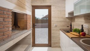 A modern kitchen with a brick oven, a wooden door leading to an outdoor area, and a countertop with a loaf of bread, vegetables, and a wine bottle. - Malibu Eclipse (Vir)