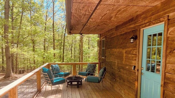 A wooden cabin with a deck, a blue door, and outdoor seating with cushions.