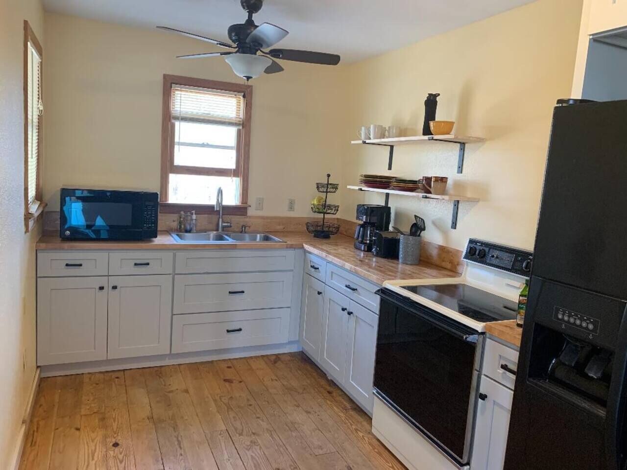 Una cocina con armarios blancos, microondas, estufa, fregadero y ventilador de techo.