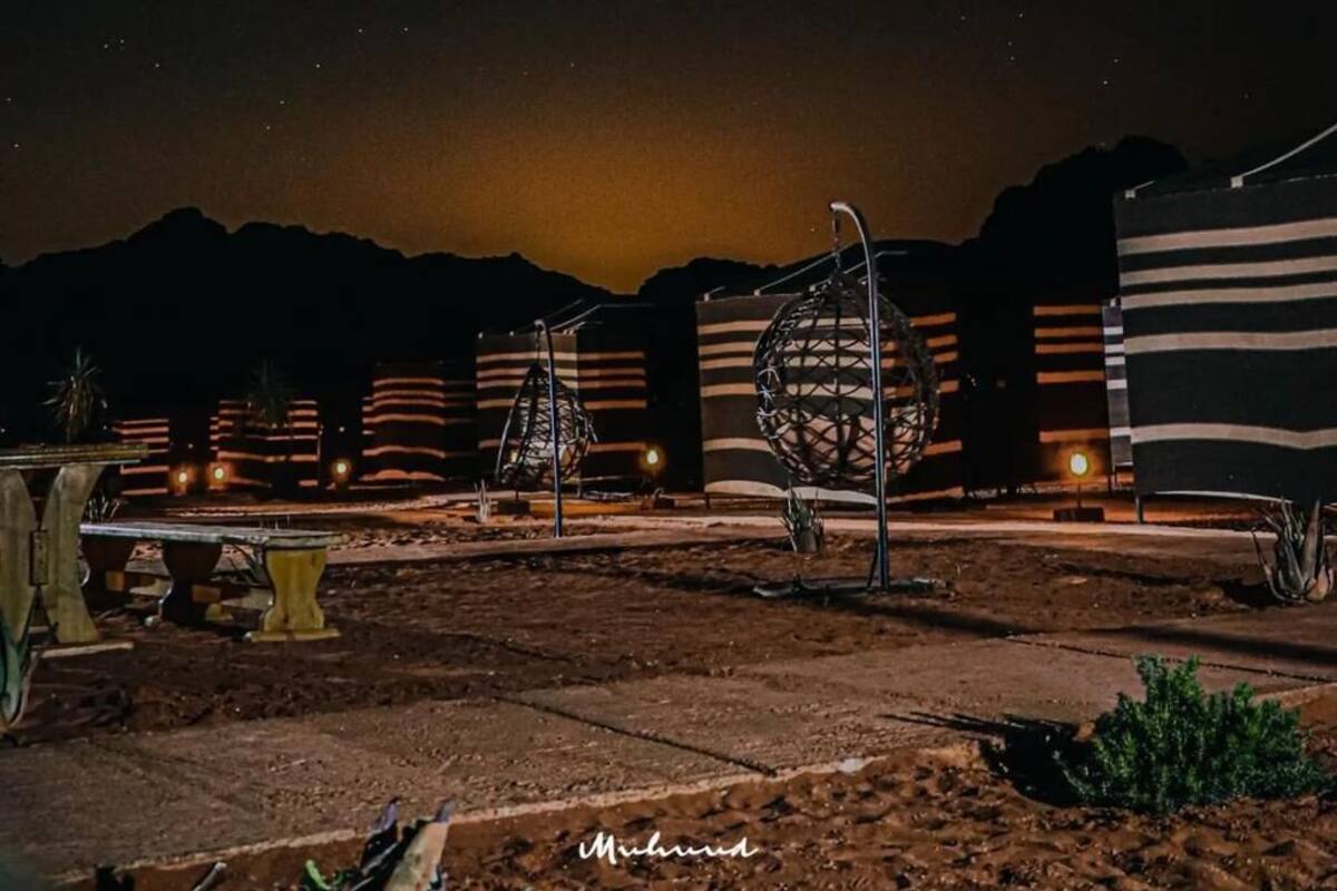 A nighttime outdoor area with a starry sky, a spherical metal sculpture, and a building with striped walls in the background.
