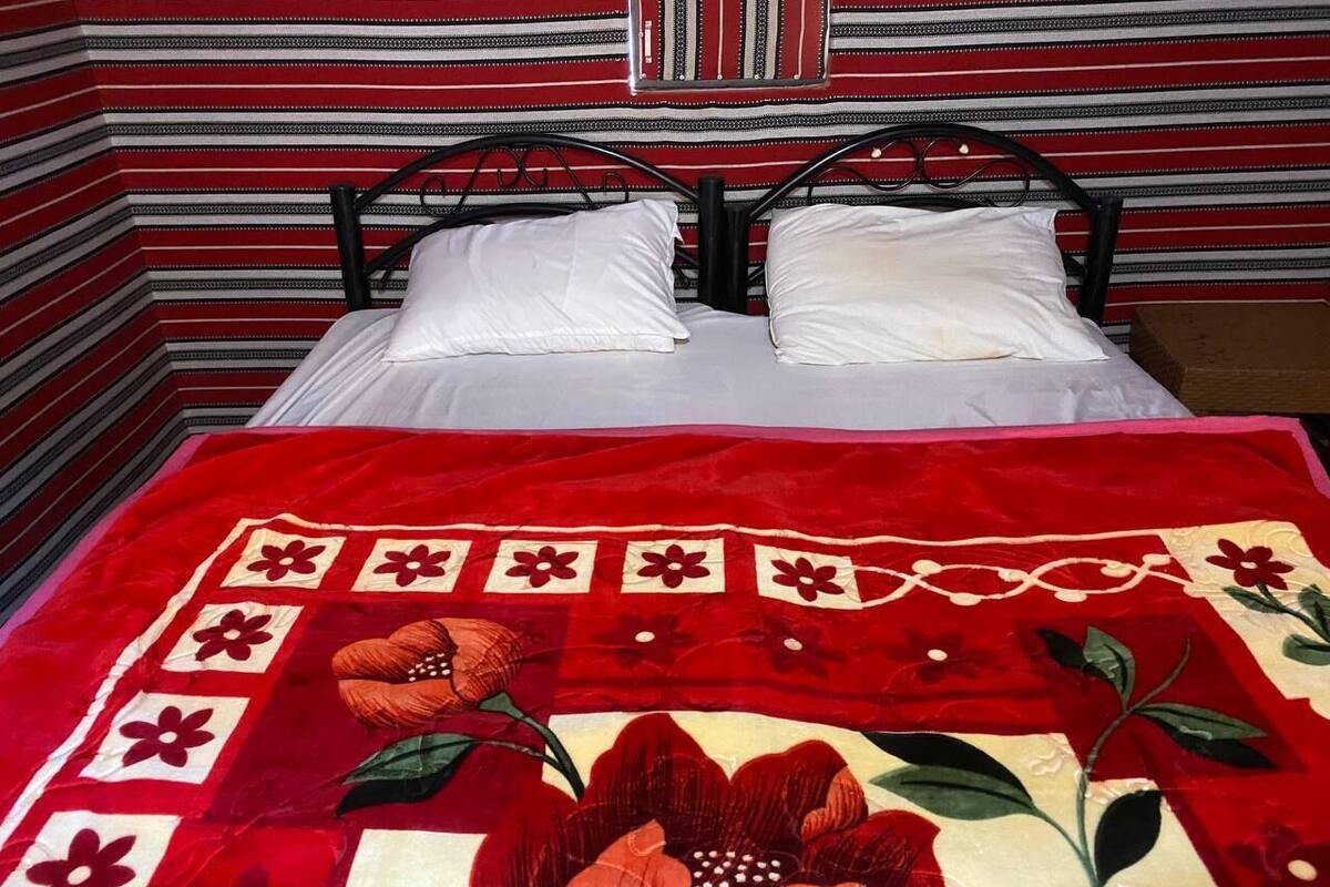 A bed with white pillows and a red floral quilt.