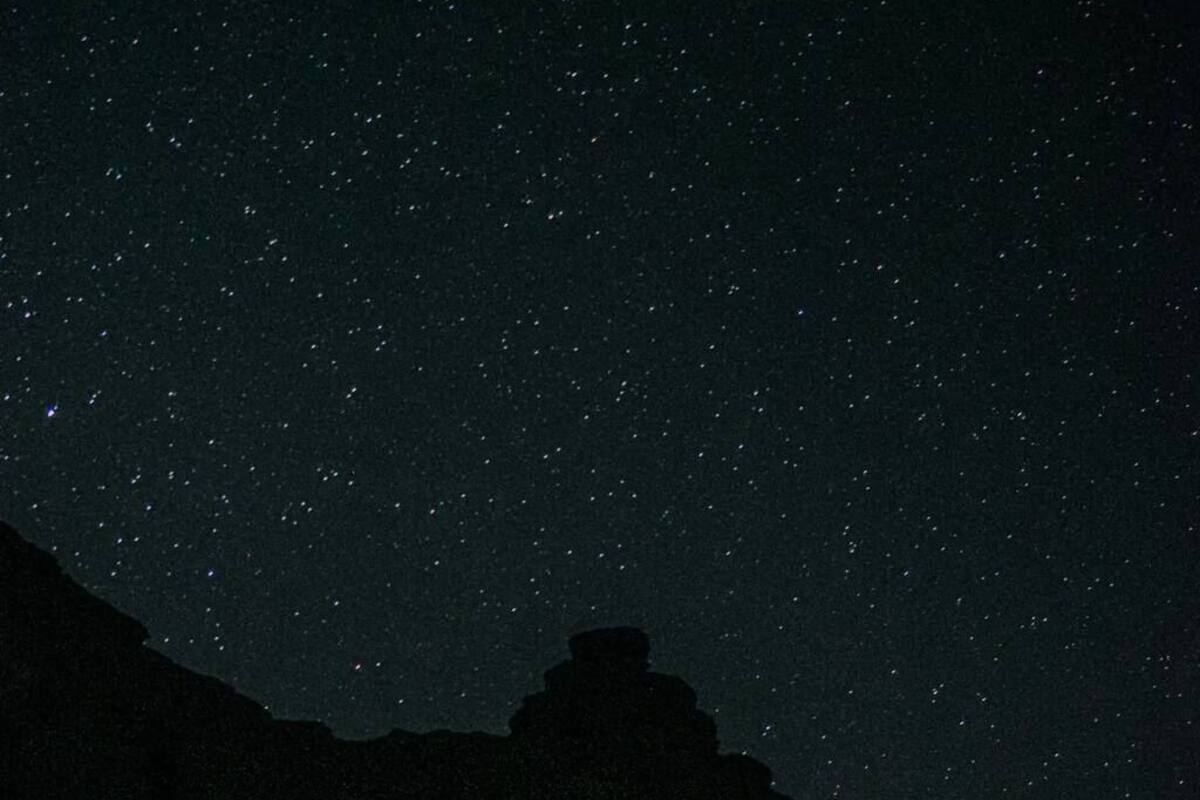A starry night sky with a large, striped tent-like structure in the foreground.