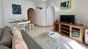 A modern living room with a sofa, dining table, TV, and decorative items. - Quarteira Central Beach by Homing (Loulé)
