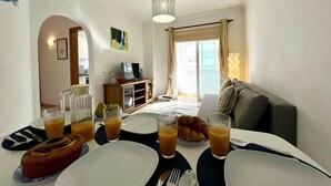 A dining area with breakfast items, a sofa, and a TV in the background. - Quarteira Central Beach by Homing (Loulé)