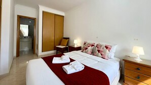 A hotel room with a bed, a wooden wardrobe, a nightstand with a lamp, and a bathroom visible through an open door. - Quarteira Central Beach by Homing (Loulé)