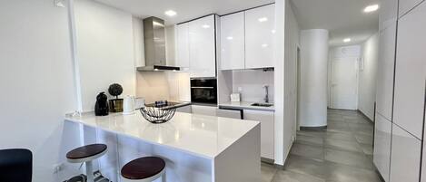 A modern kitchen with white cabinetry, a central island with stools, and a sleek design.