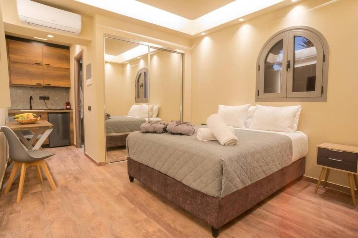 A bedroom with a bed, bedside tables, a mirror, and a view of the kitchen.