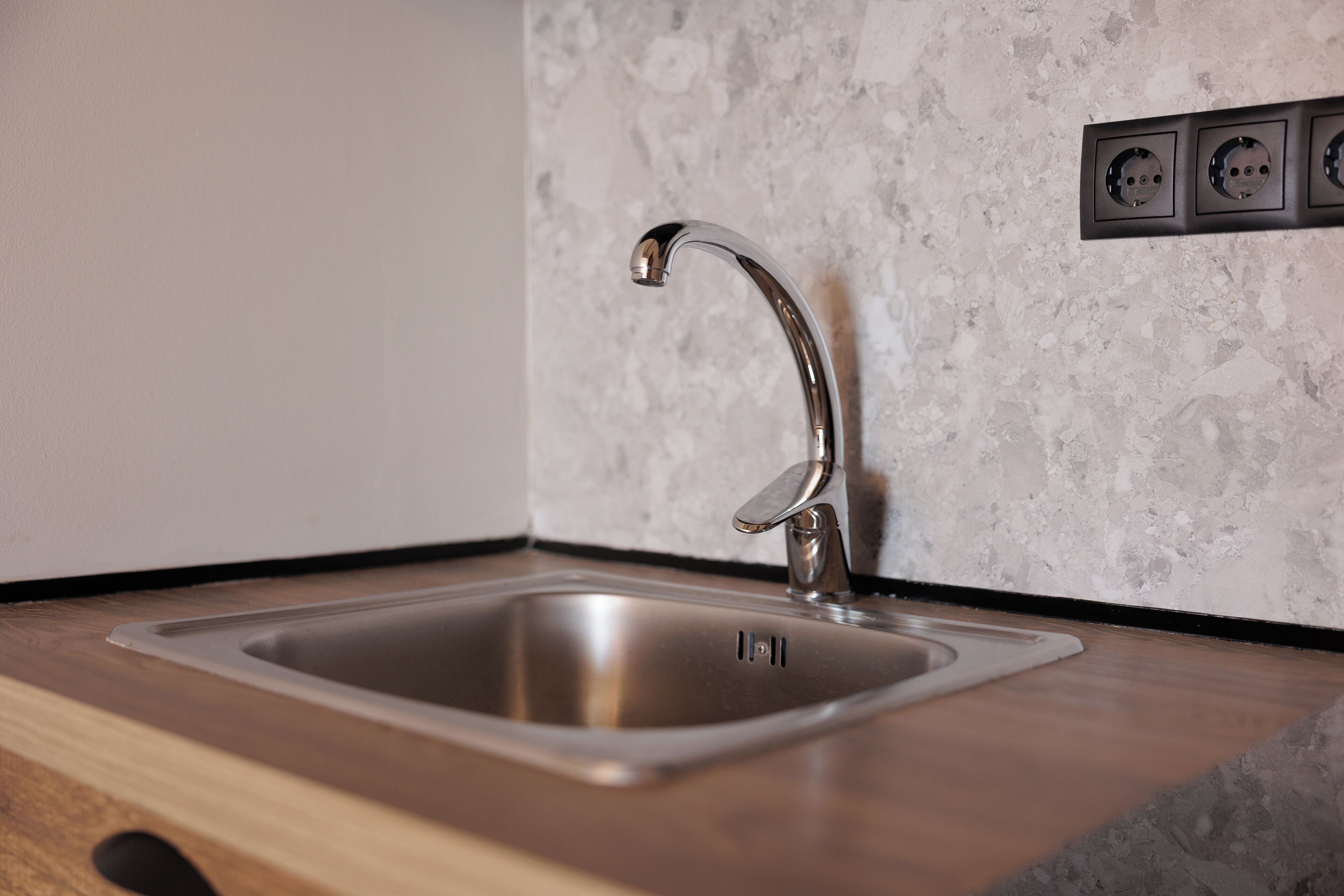 Una cucina moderna con lavello in acciaio inossidabile, piano di lavoro in legno e parete strutturata.
