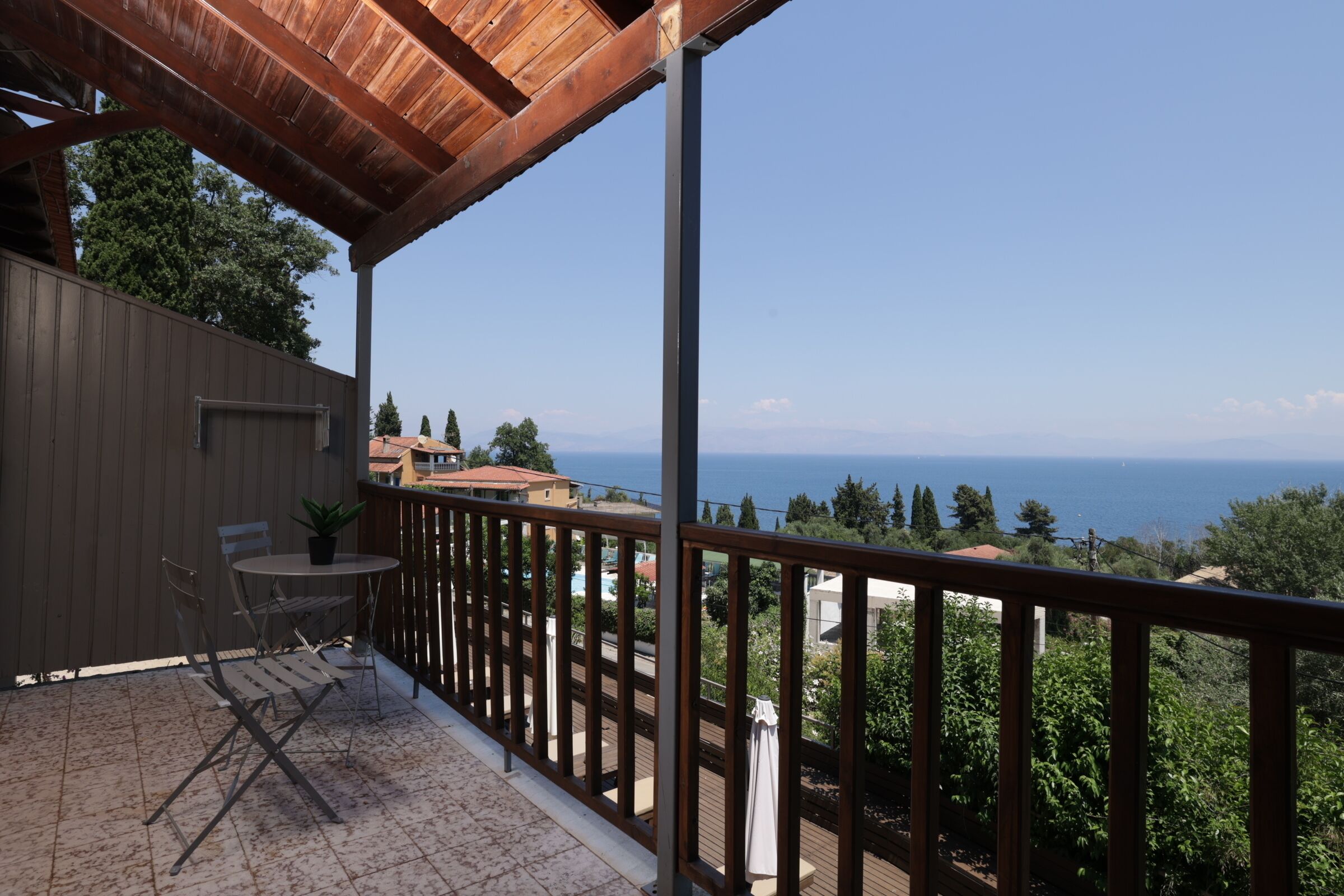 A balcony with a view of the sea, a table with chairs, and a potted plant.
