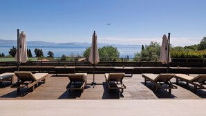 Une terrasse dotée de chaises longues et de parasols, offrant une vue sur un plan d’eau et des montagnes.