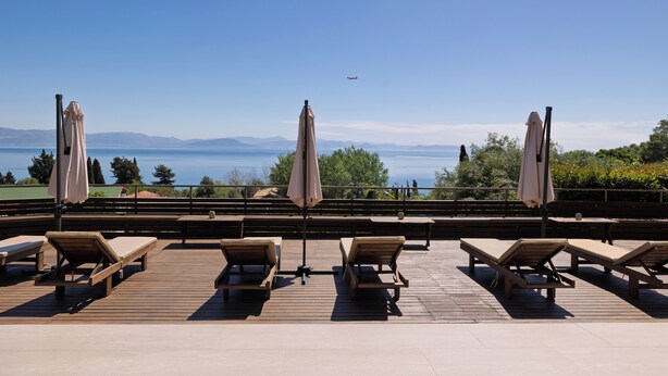 Una terrazza con sedie a sdraio e ombrelloni che si affaccia su un lago e montagne.