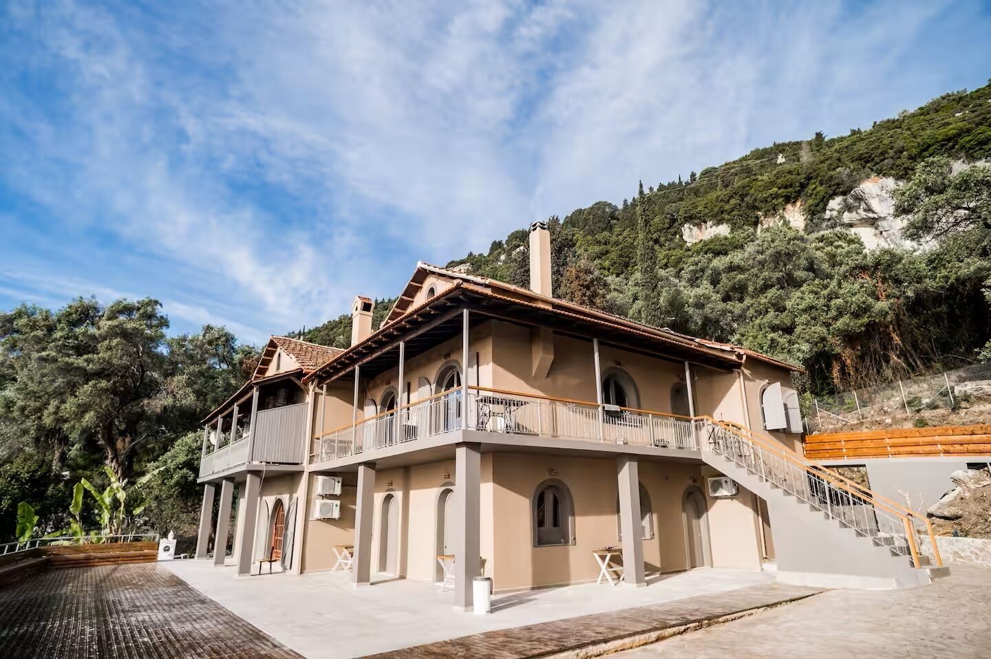 Un edificio de dos plantas con balcones, una escalera y vistas a una ladera boscosa.