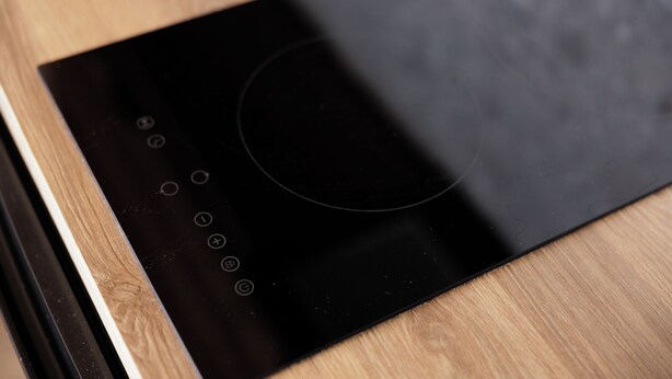 Une plaque de cuisson à induction noire, dotée de boutons de commande et d’un pavé tactile circulaire, le tout posé sur une surface en bois.