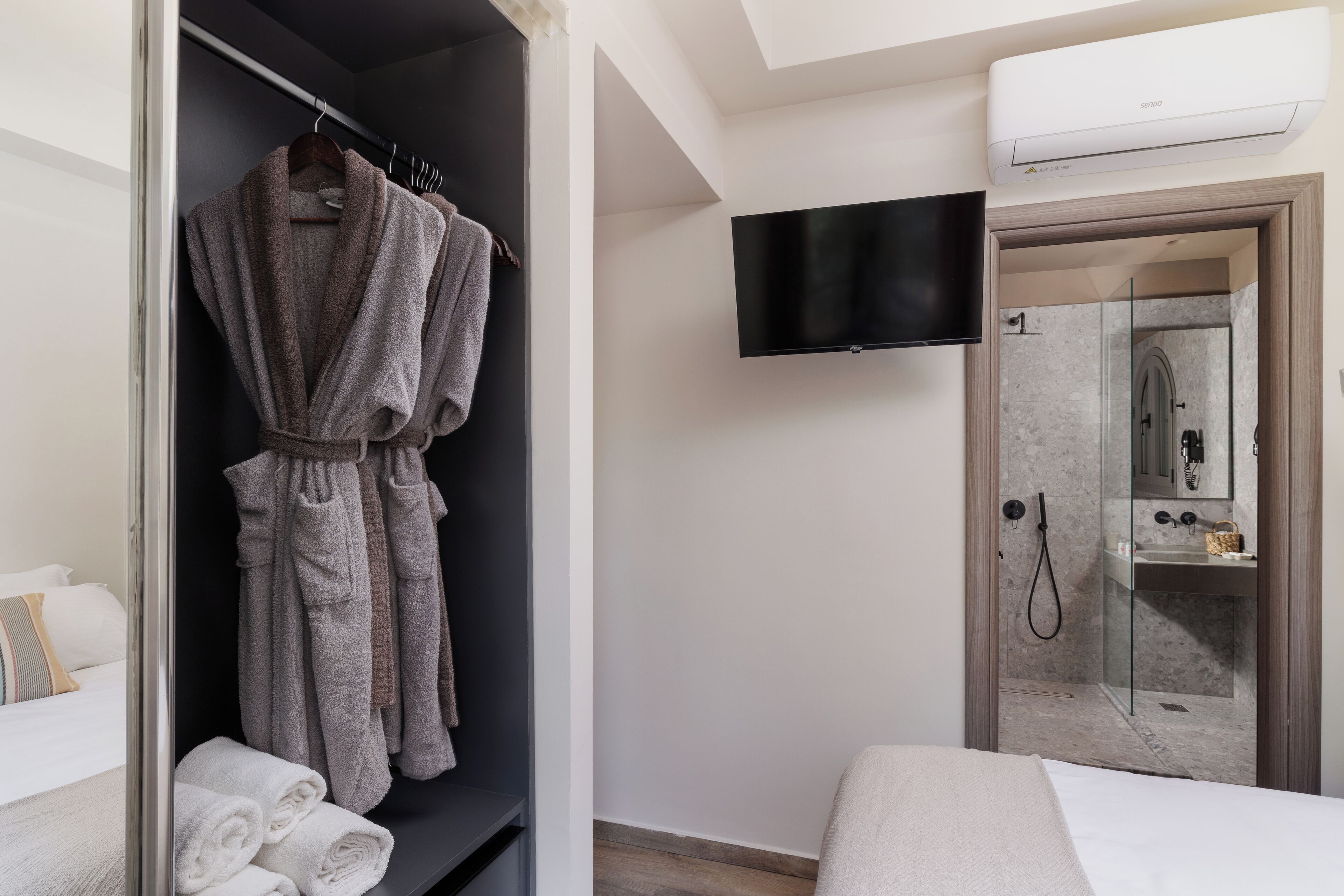 A hotel room with a walk-in closet, a bed, a TV, and a shower area.