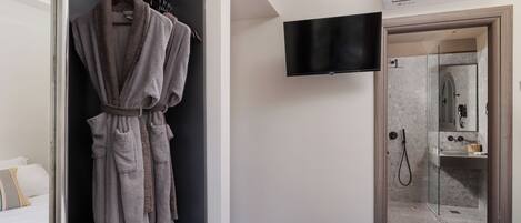 A hotel room with a walk-in closet, a bed, a TV, and a shower area.
