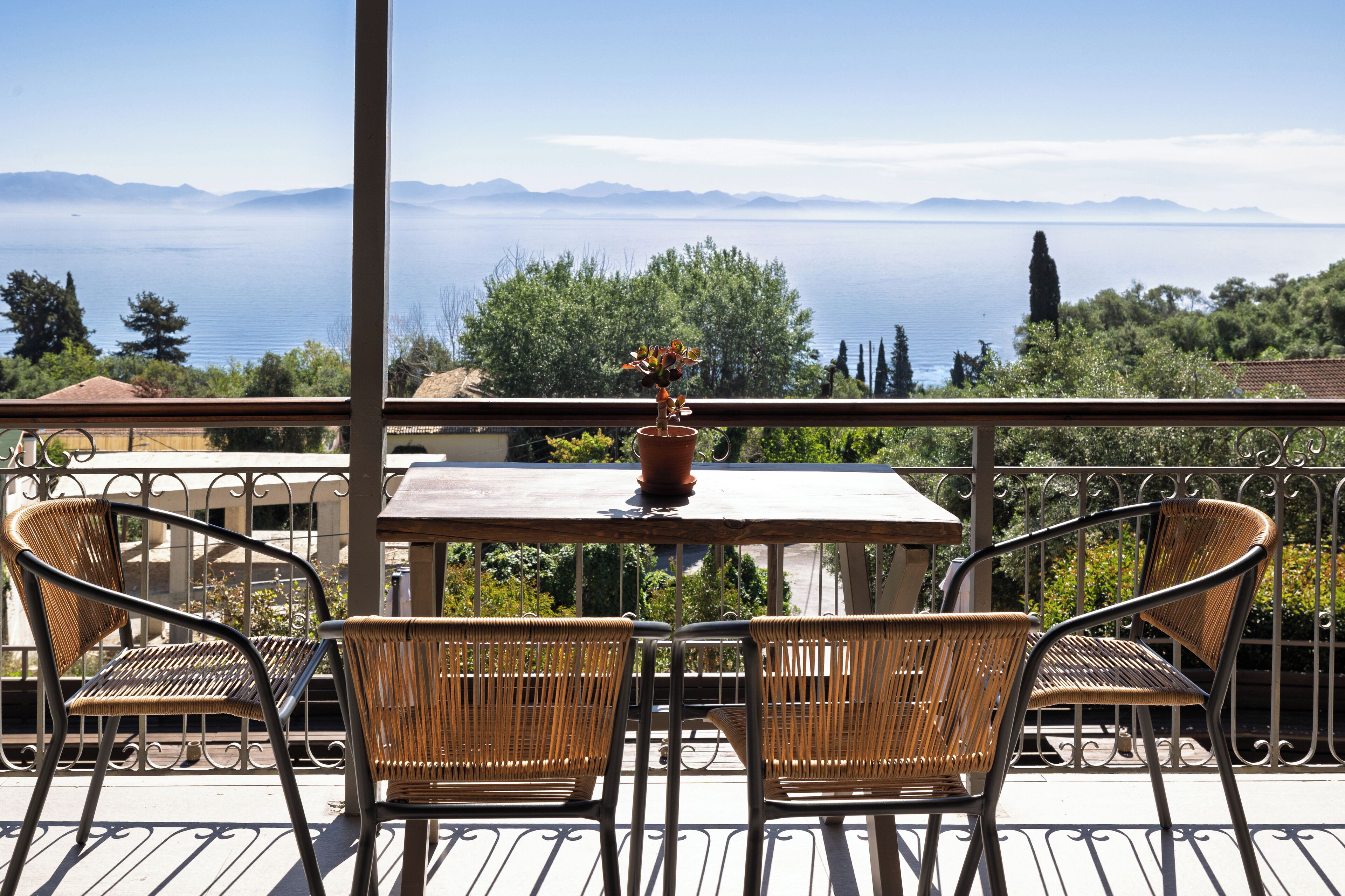 Un balcon avec des fauteuils en osier, une table et un pot de fleurs.