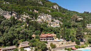 Una proprietà su una collina con una grande casa dotata di piscina, immersa nel verde e tra rocce.