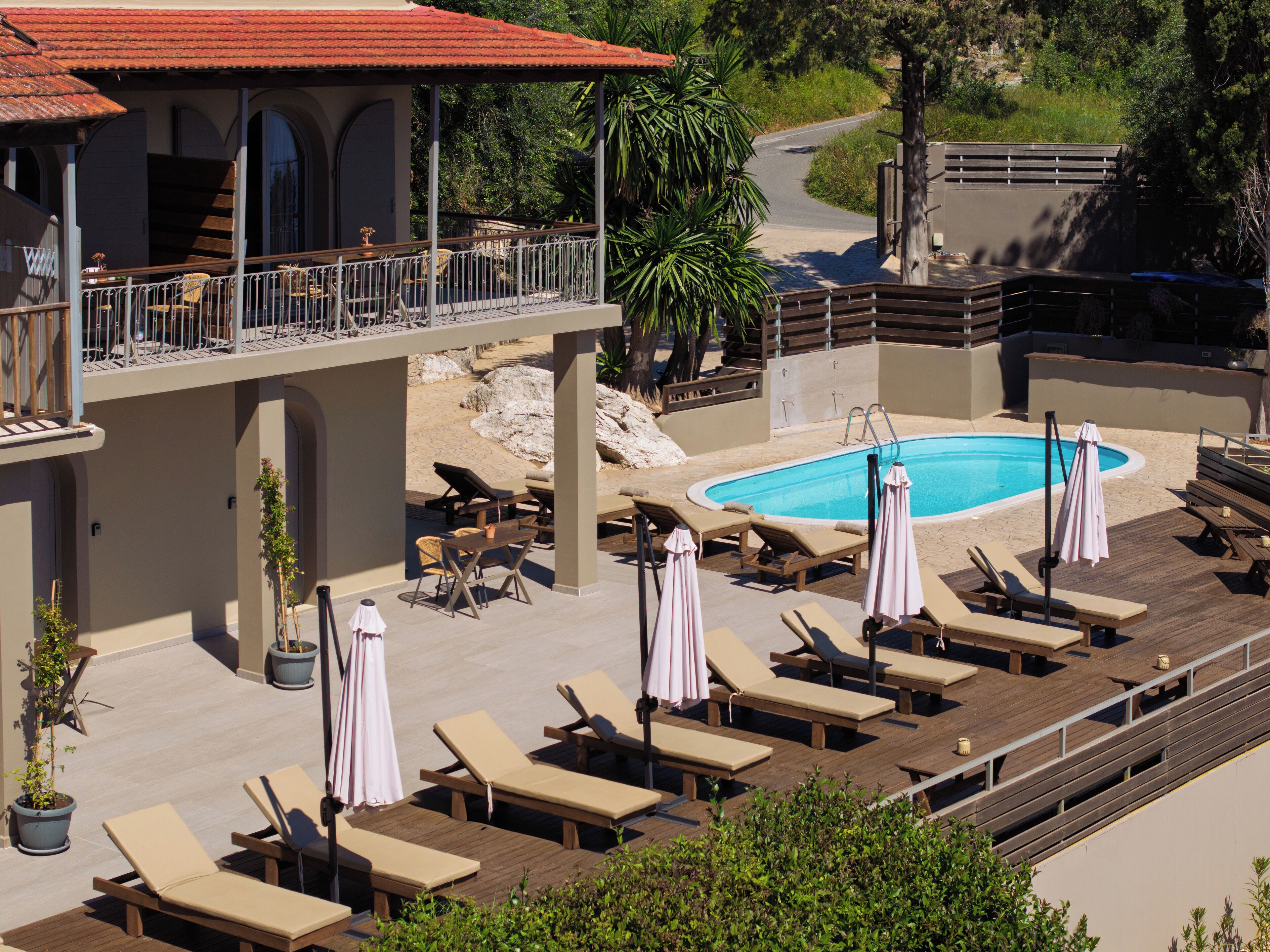 Zona de piscina con sillones de descanso y sombrillas, una piscina y un edificio con tejado de tejas rojas.
