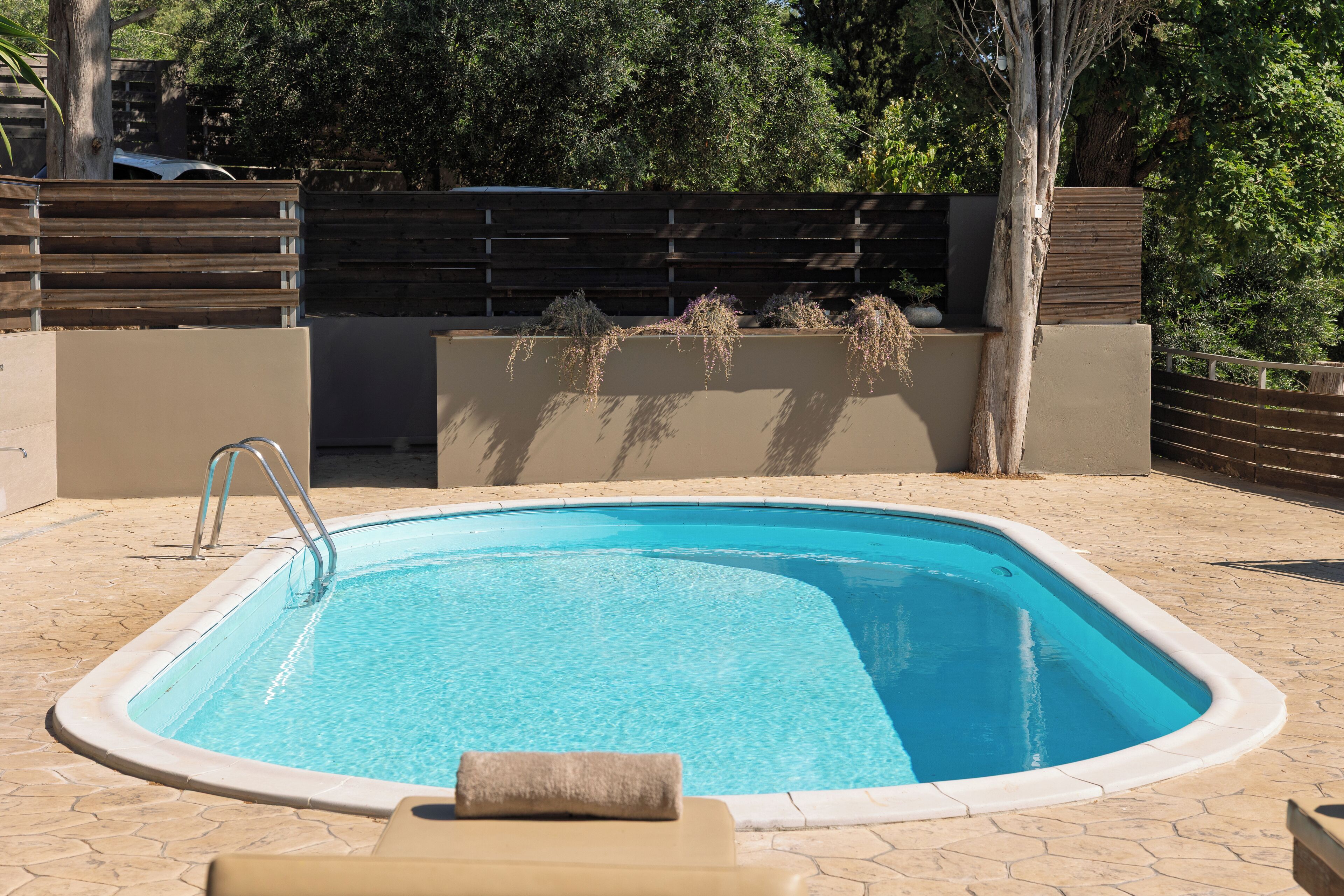 A rectangular swimming pool with a metal ladder, surrounded by a tiled patio.