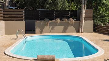 A rectangular swimming pool with a metal ladder, surrounded by a tiled patio.